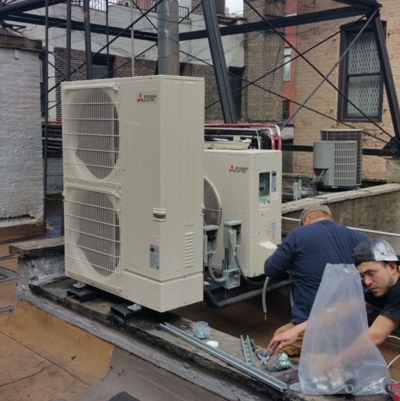 Two men installing a Mitsubishi HVAC system on the roof of a building