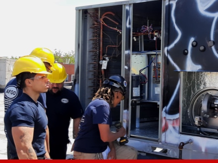 Four men with safety hats inspecting rooftop HVAC system