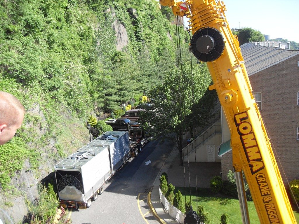 A man leans over edge of building while watching yellow crane