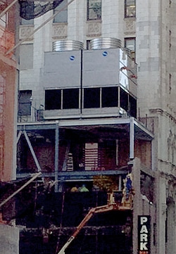 Cooling tower and HVAC system being installed on rooftop of building while a man is being lifted by a crane