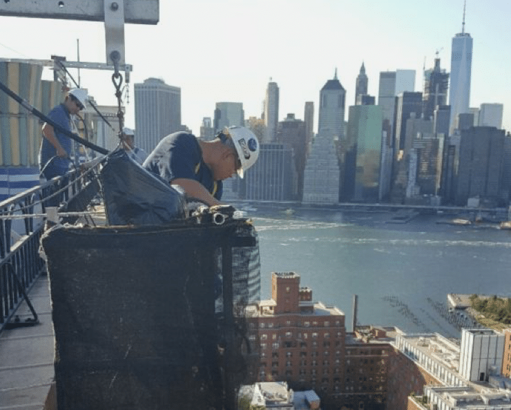 Man looking over edge of building while guiding crane for rooftop HVAC installment